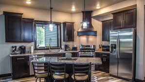 A modern kitchen with dark wood cabinets, stainless steel appliances, and a central island with bar stools. - Beautiful Getaway! All paved roads, garage, Snowmobile, Terry Peak, Deadwood (Lead)