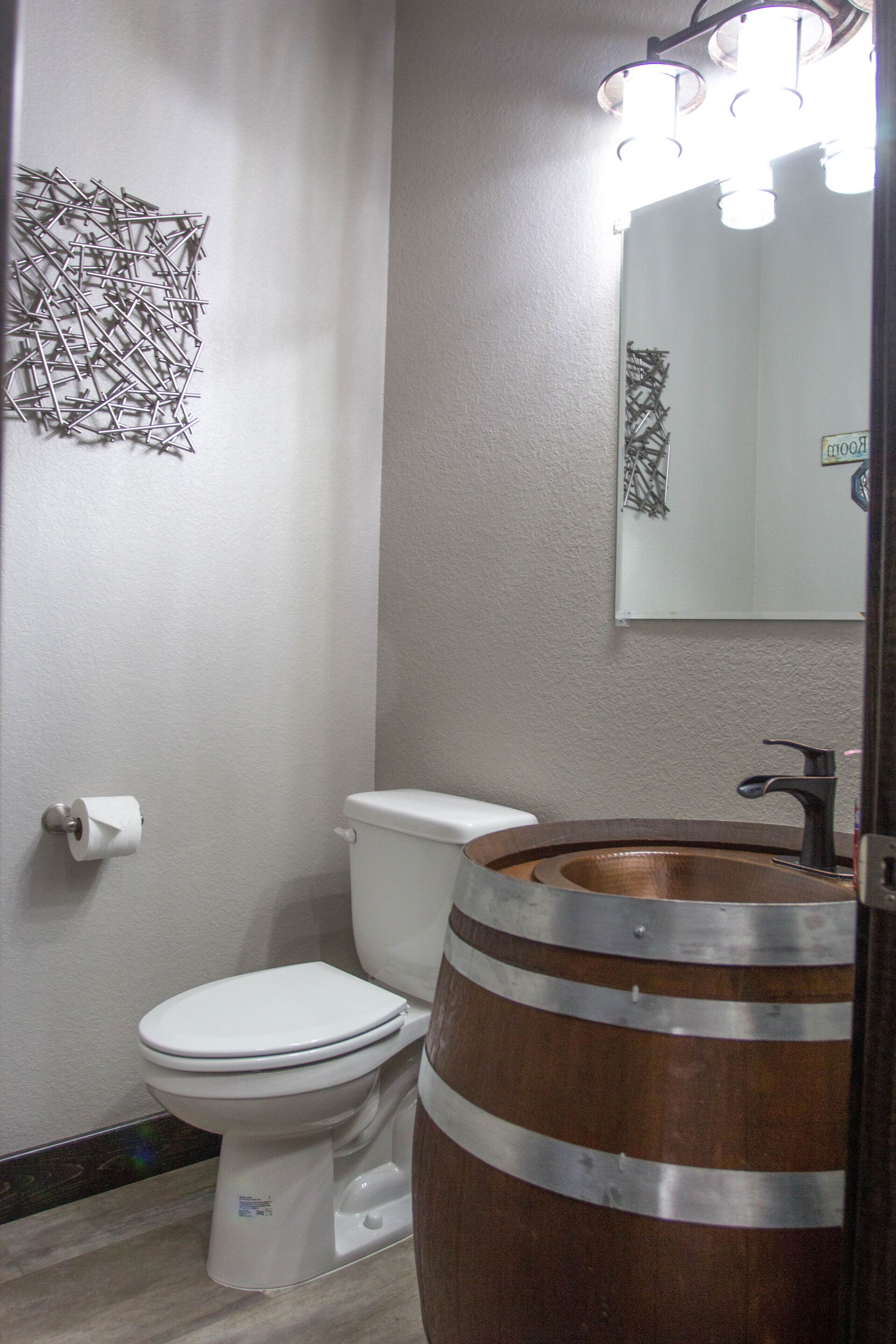 Un baño con inodoro blanco, lavamanos de barril de madera y un espejo con iluminación.