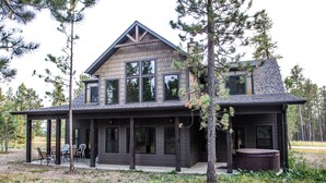 A two-story log cabin with a covered porch, large windows, and a hot tub. - Beautiful Getaway! All paved roads, garage, Snowmobile, Terry Peak, Deadwood (Lead)