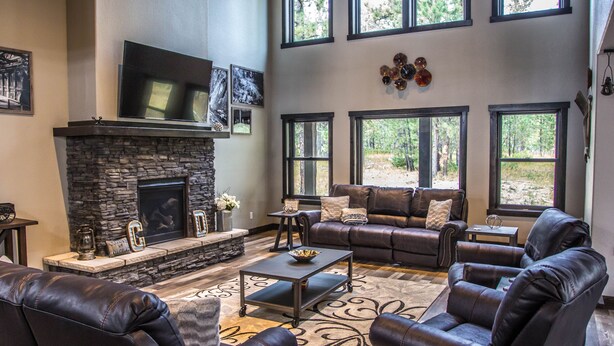 A spacious living room with a stone fireplace, leather sofas, and large windows offering a view of the outdoors. - Beautiful Getaway! All paved roads, garage, Snowmobile, Terry Peak, Deadwood (Lead)