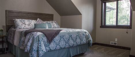 A bedroom with a sloped ceiling, a large bed with patterned bedding, a nightstand, and a window with blinds.