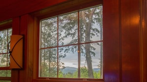 Une cabane dotée de grandes fenêtres, d’un intérieur en bois et offrant une vue sur une forêt et des montagnes.