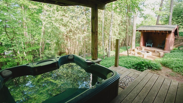 Un bain à remous sur une terrasse en bois, avec vue sur une forêt et un petit chalet.