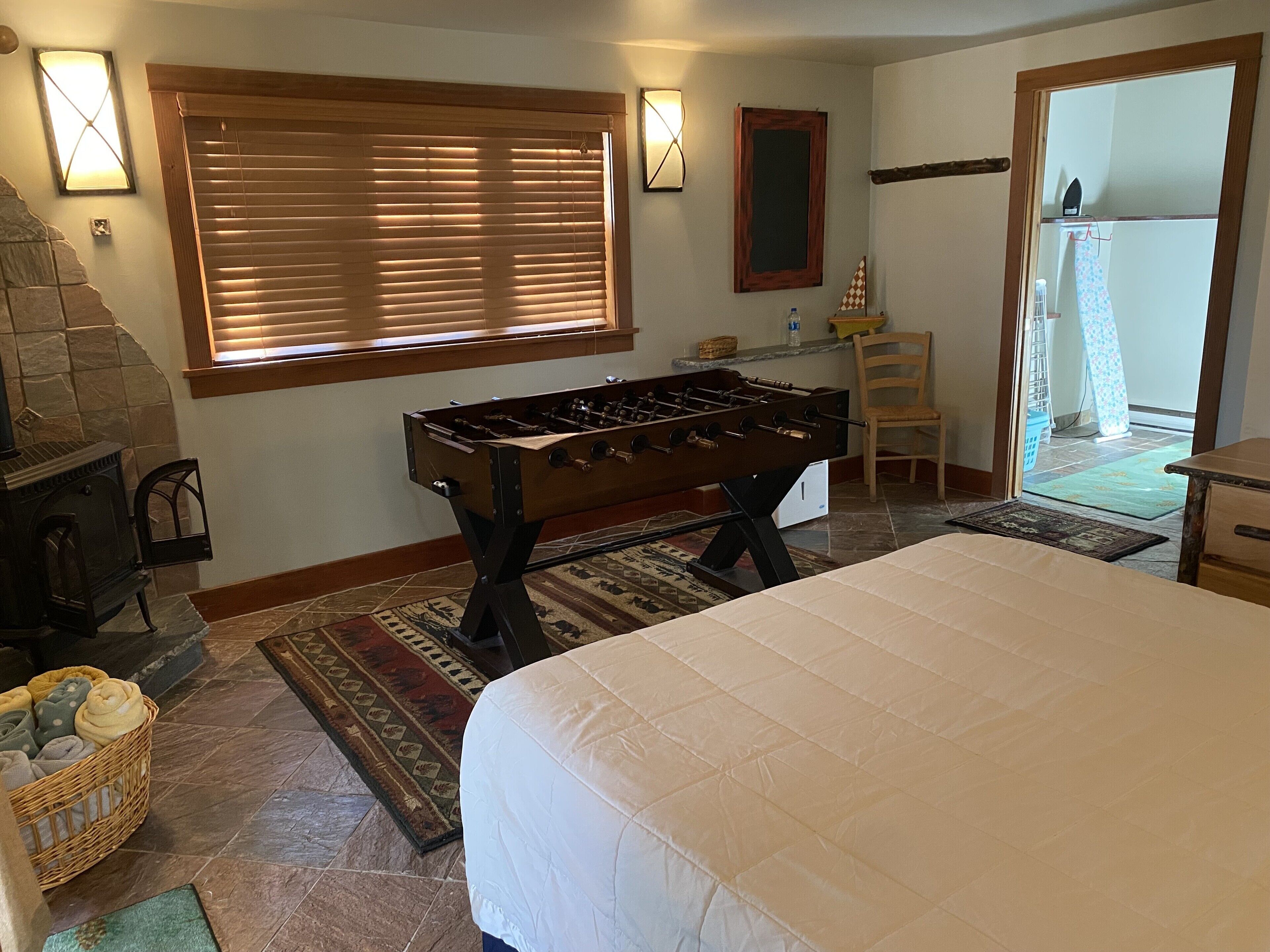 A room with a foosball table, a fireplace, a large bed, and a view through a glass door.