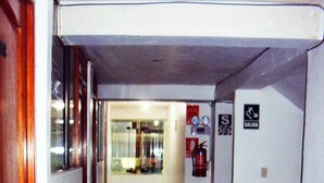 Un pasillo estrecho con suelo de baldosas azul oscuro, una puerta de madera a la izquierda y un extintor a la derecha.