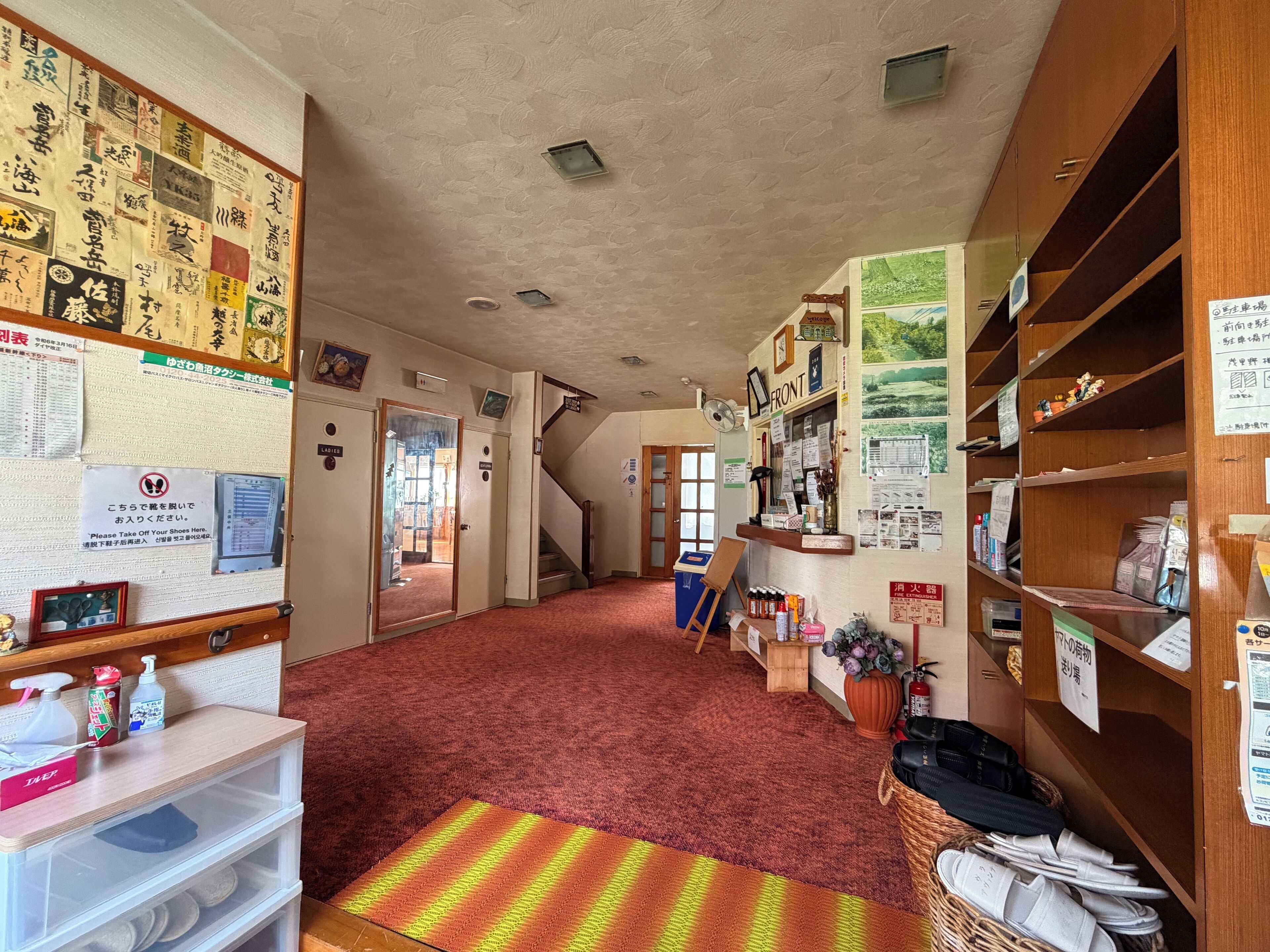 Una hall d'albergo con tappeto rosso, scaffali in legno e una bacheca con diversi avvisi.
