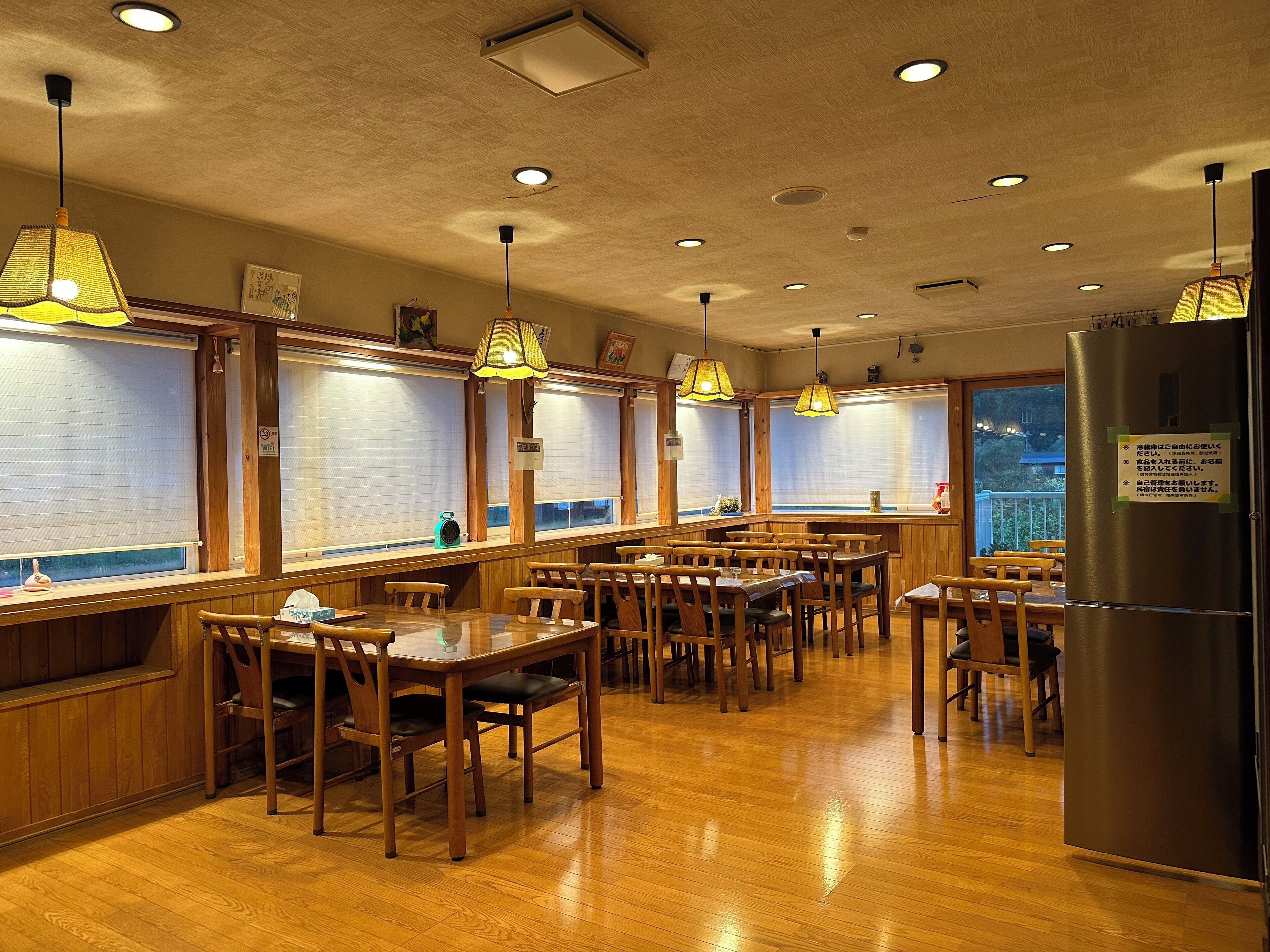 Un restaurant avec des tables et des chaises en bois, des lampes suspendues et un réfrigérateur.