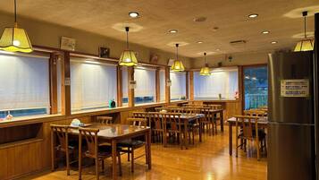 A restaurant with wooden tables and chairs, hanging lamps, and a refrigerator.