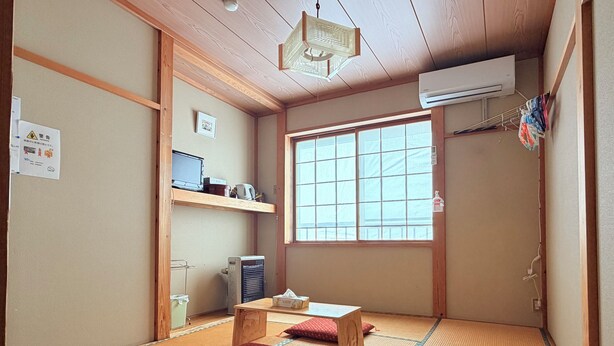 A traditional Japanese room with tatami flooring, a futon bed, a desk with a computer, and a large window. - Kagura House (Yuzawa)