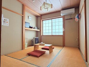 A traditional Japanese room with tatami flooring, a futon bed, a desk with a computer, and a large window. - Kagura House (Yuzawa)