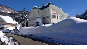 A building with a sign in Japanese, surrounded by snow-covered terrain and mountains in the background. - Kagura House (Yuzawa)
