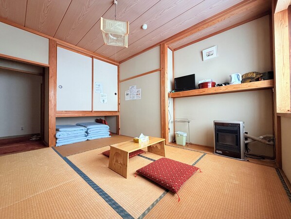 A traditional Japanese room with tatami flooring, a low wooden table, a red cushion, a television, and a heater. - Kagura House (Yuzawa)