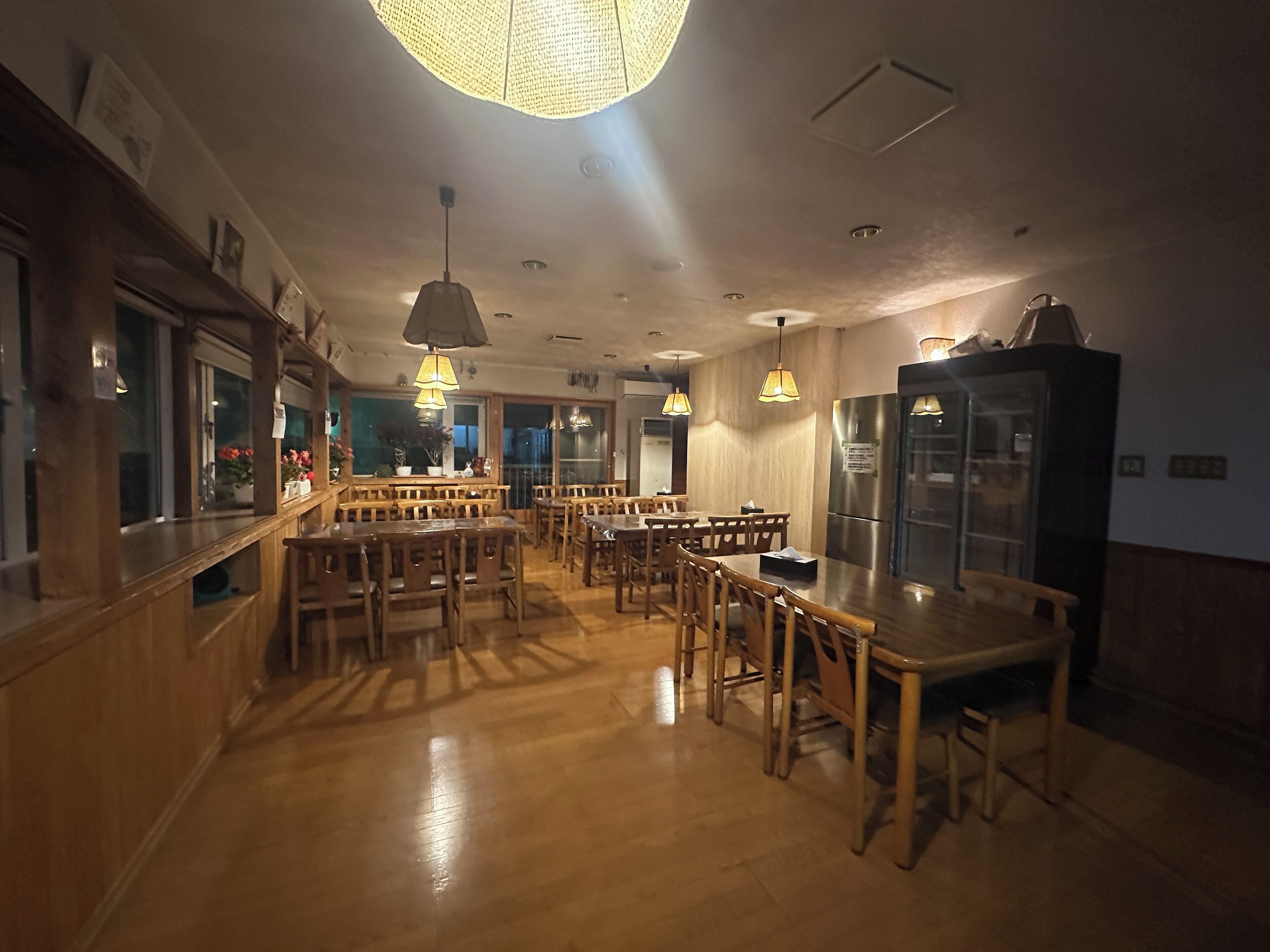 A restaurant with wooden tables and chairs, a bar area, and a large refrigerator.