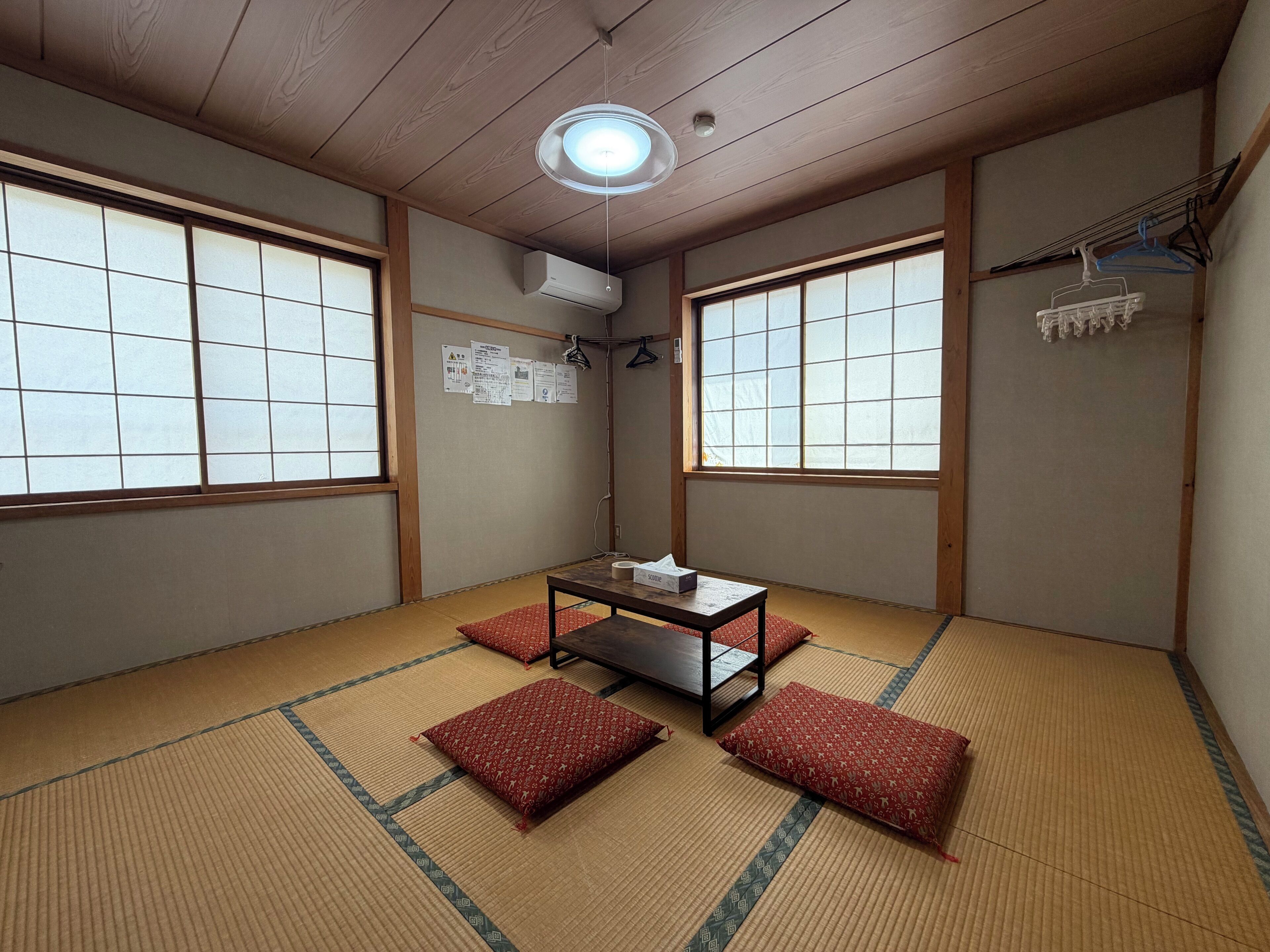 A traditional Japanese room with tatami flooring, a low table, and red cushions.