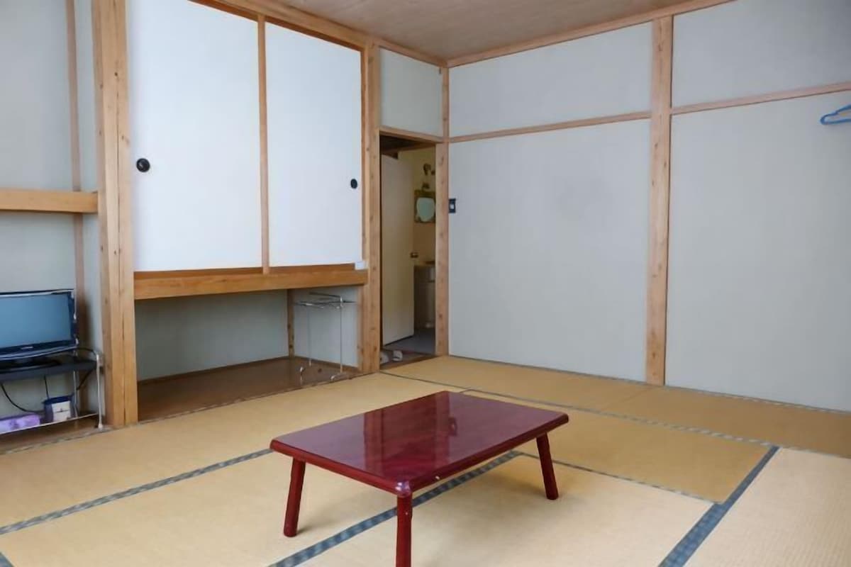 Una habitación con tatami, una mesa de madera, puertas correderas y un televisor sobre un mueble.