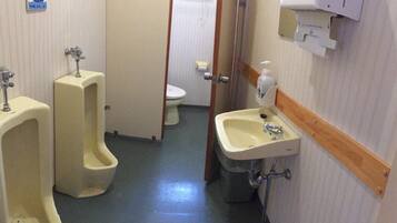 Um banheiro masculino com dois mictórios, um vaso sanitário e uma pia com dispensador de sabonete.