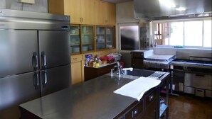 A commercial kitchen with stainless steel appliances, wooden cabinets, and a large work counter. - Kagura House (Yuzawa)