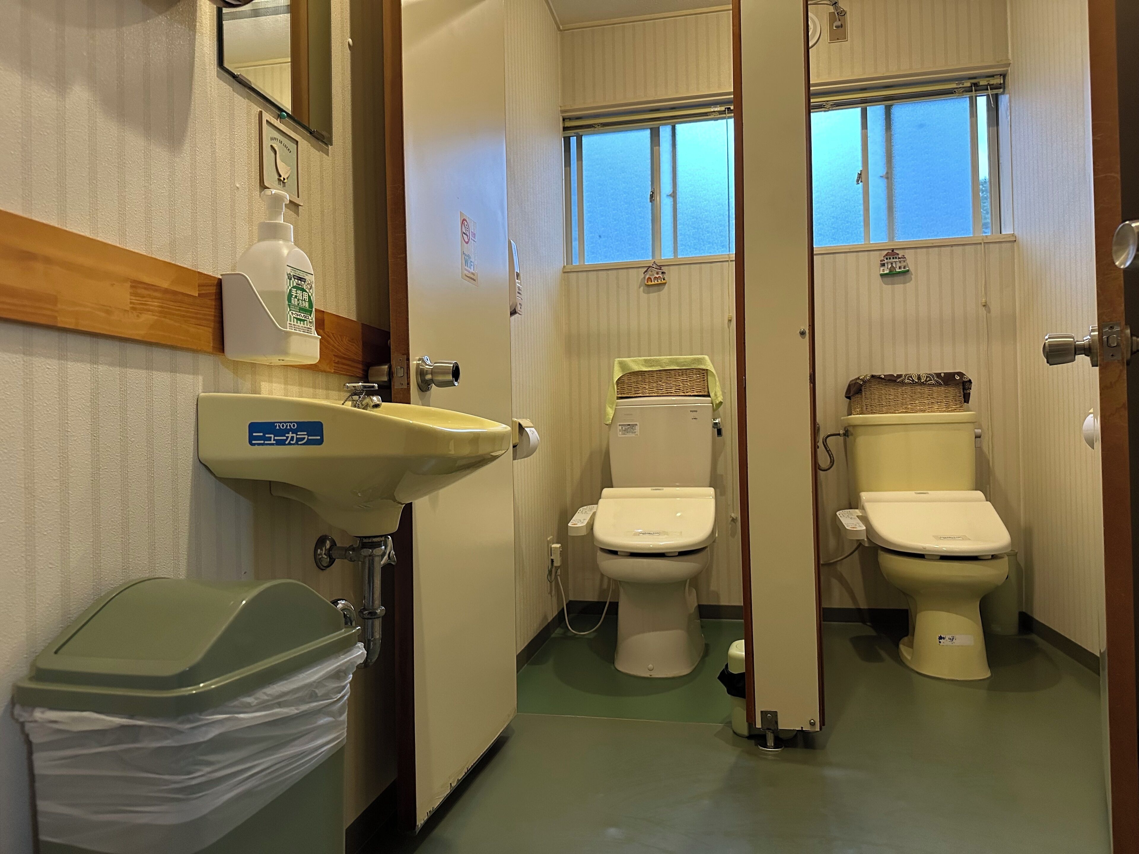 A bathroom with two toilets, a sink, and a trash bin.