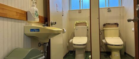 A bathroom with two toilets, a sink, and a trash bin.