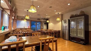 A restaurant with wooden tables and chairs, hanging pendant lights, and a refrigerator. - Kagura House (Yuzawa)