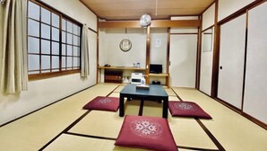 Una habitación japonesa tradicional con suelo de tatami, una mesa baja, cojines, un televisor y un ventilador de techo.