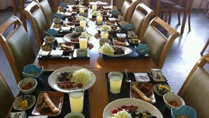 Una mesa de comedor dispuesta con diversos platos, incluyendo porciones de comida, tazones y vasos de jugo.