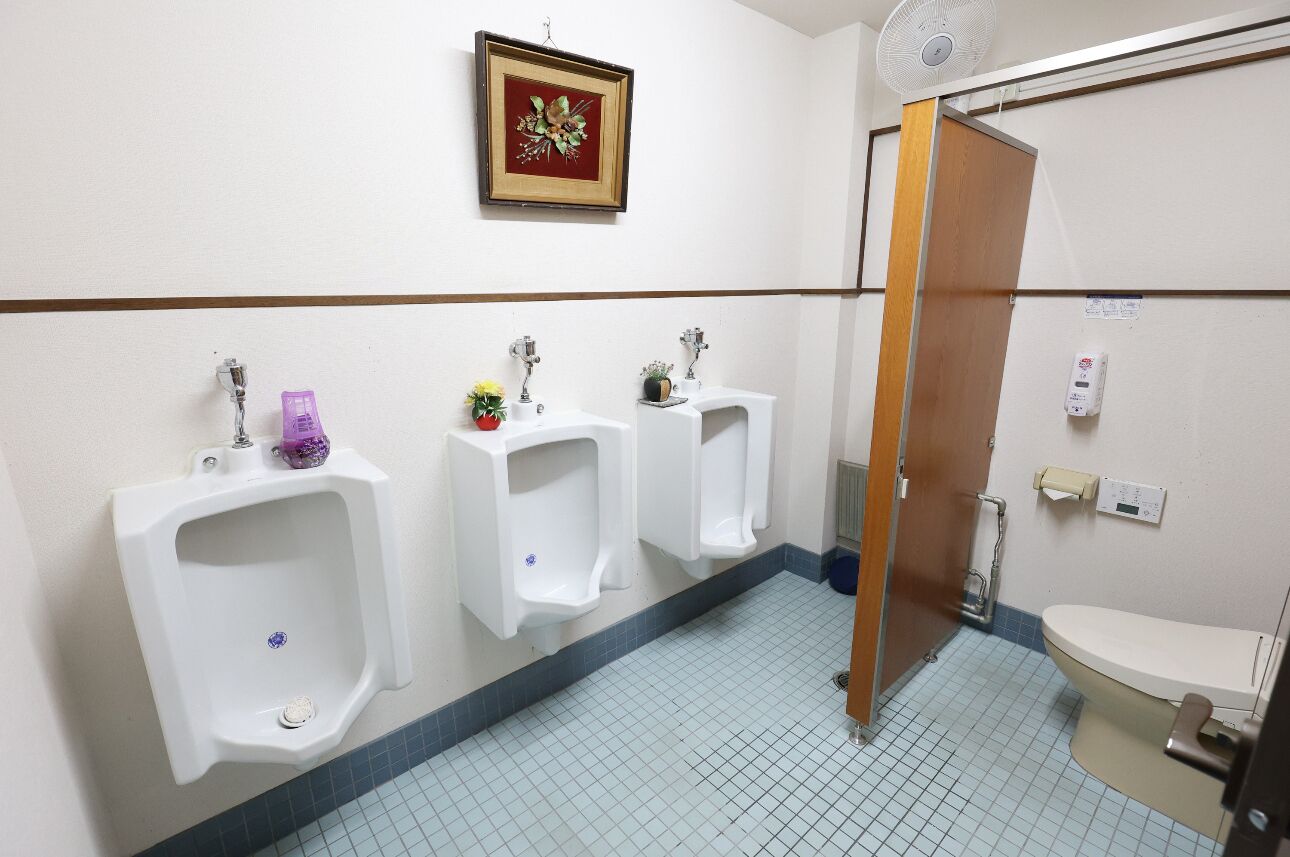A men's restroom with urinals, a toilet, a hand dryer, and a wall-mounted fan.
