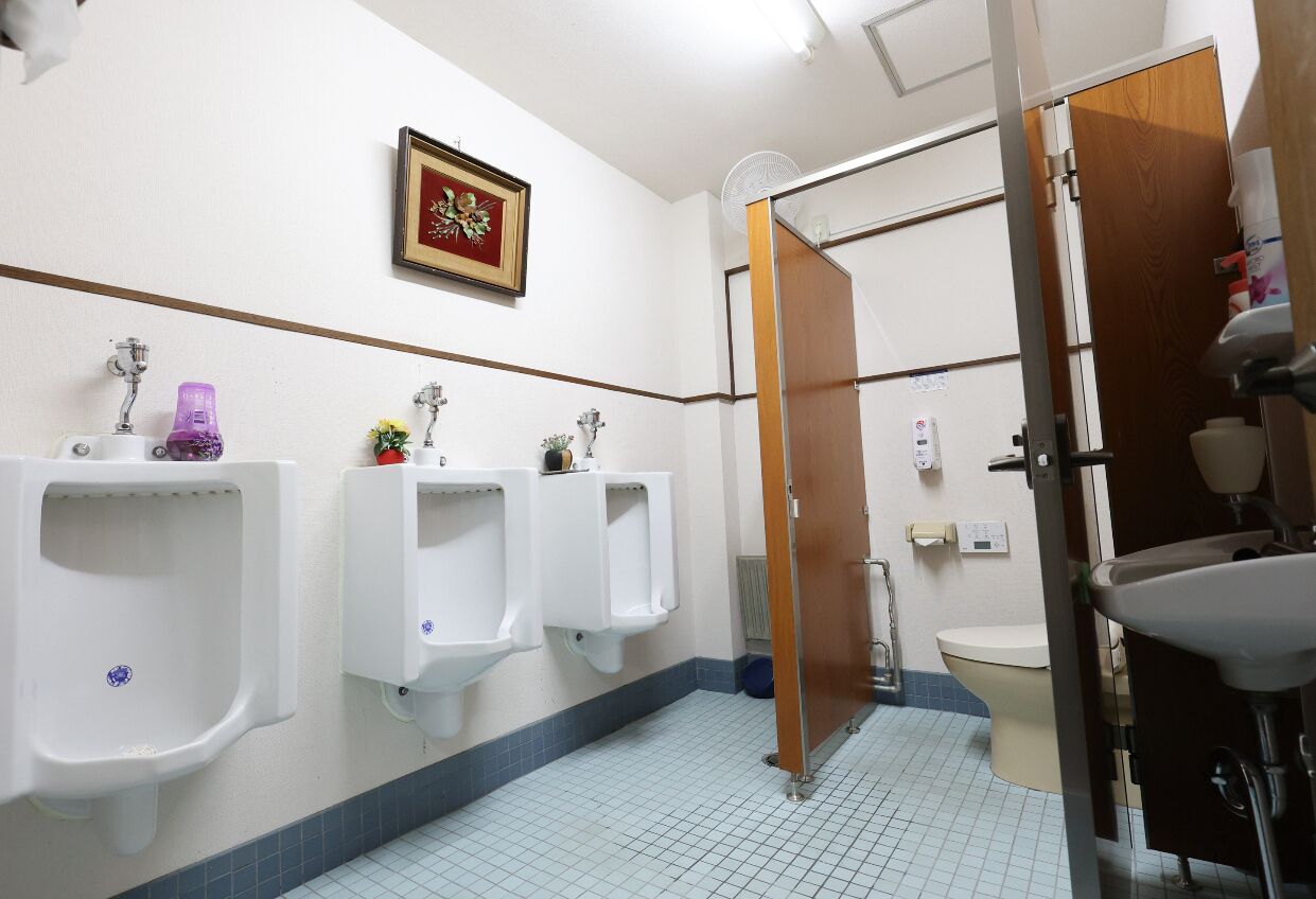 A public restroom with urinals, a toilet, a sink, and a fan.