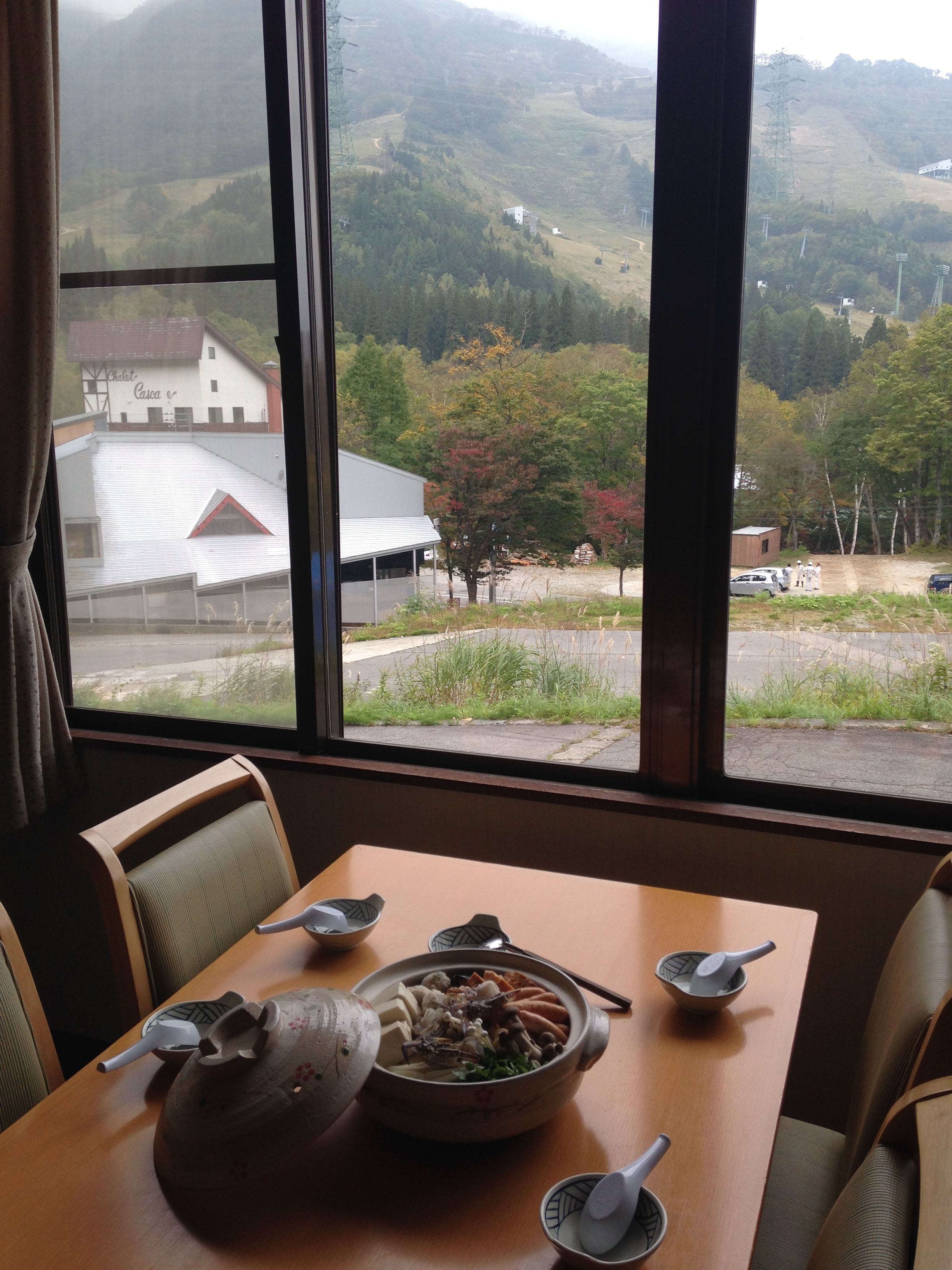 A dining table with a traditional meal setup, a view of a rural landscape through a window, and a building with a red roof in the background.