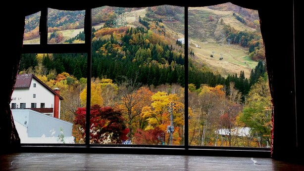 Habitación con un amplio ventanal que ofrece vistas a un paisaje montañoso con follaje otoñal.