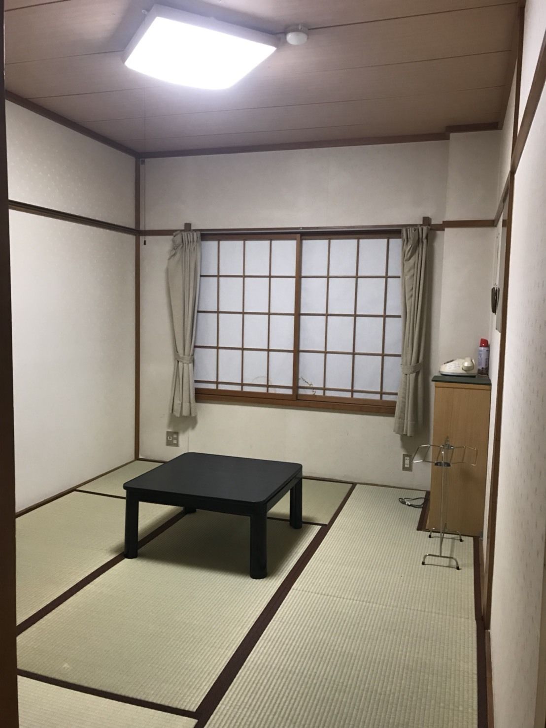 A traditional Japanese room with tatami flooring, a low table, a window with shoji screens, and a cabinet with a telephone.