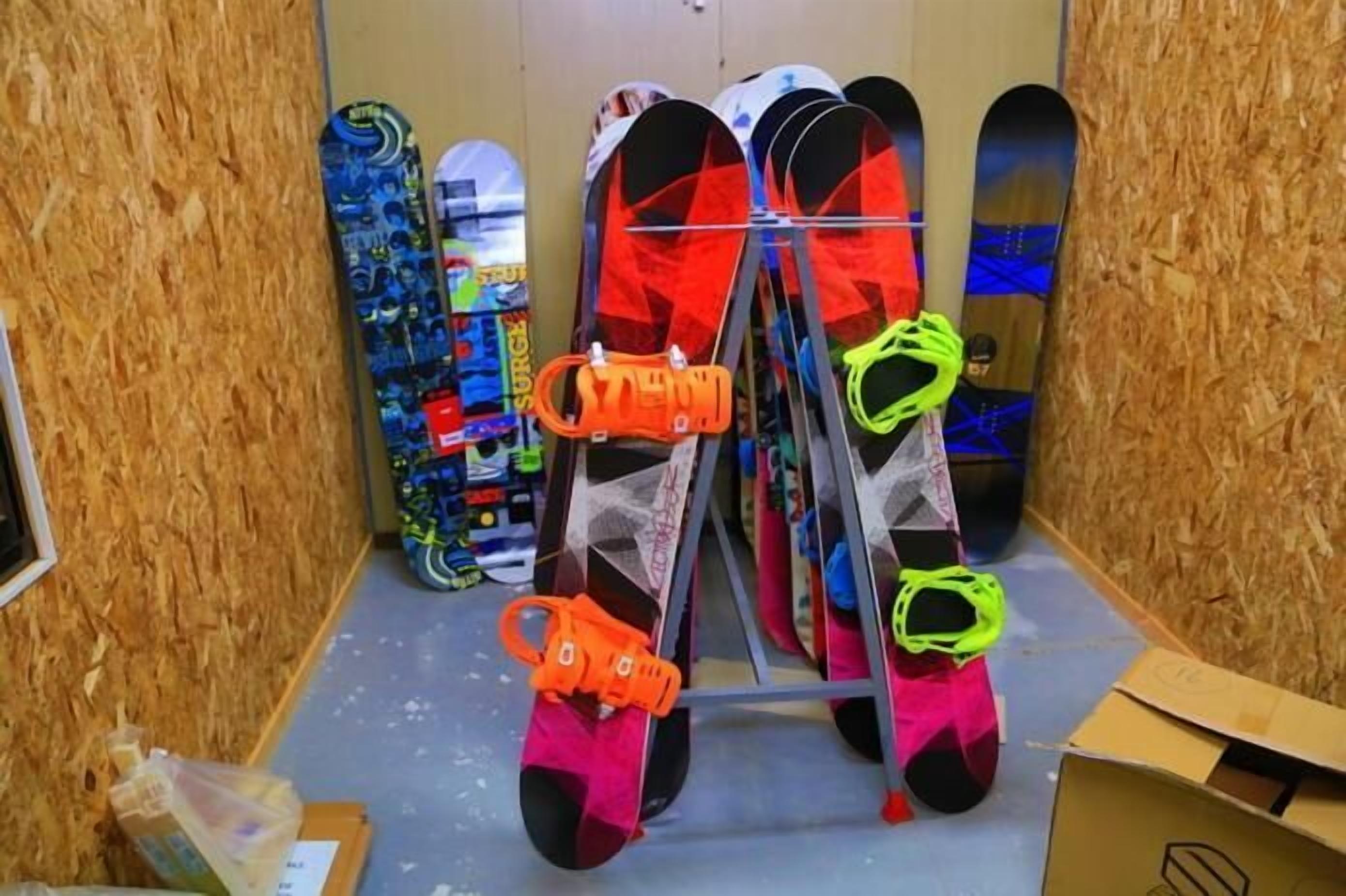 A room with a wooden wall, a metal rack holding skis, and a snowboard leaning against the wall.