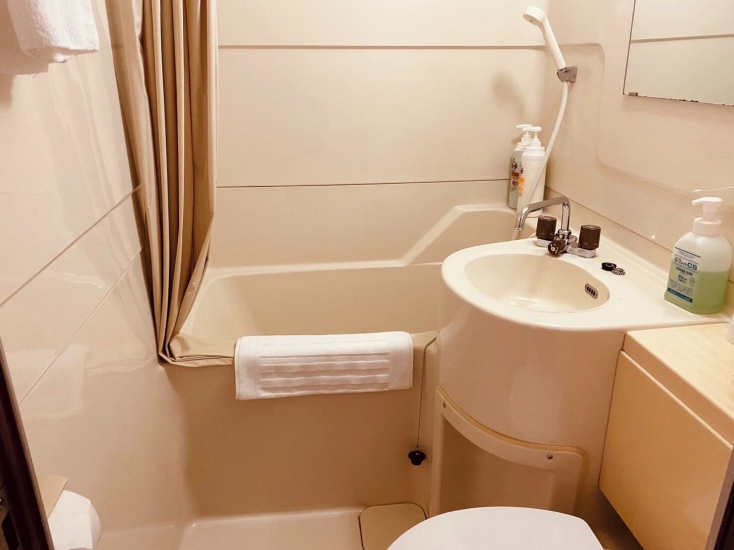 A small, compact bathroom with a bathtub, a sink, and a toilet. There is a towel hanging on the wall, and toiletries are placed on the sink counter.