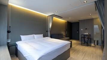 A modern hotel room with a large bed, bedside tables, a desk, and a small seating area.