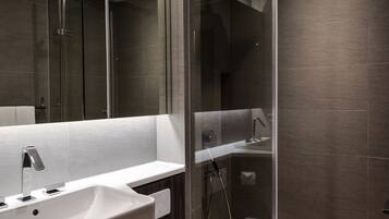 A modern bathroom with a large mirror, a white sink, a shower enclosure, and a toilet.