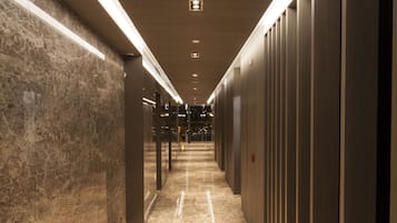 A corridor with a marble floor, curved lighting, and a row of lockers on one side.