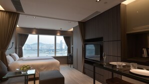 Een moderne hotelkamer met een groot bed, een televisie, een zithoek en uitzicht op de stad.