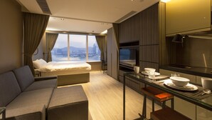 Een moderne hotelkamer met een groot bed, een bank, een eethoek met een glazen tafel en uitzicht op de stad.