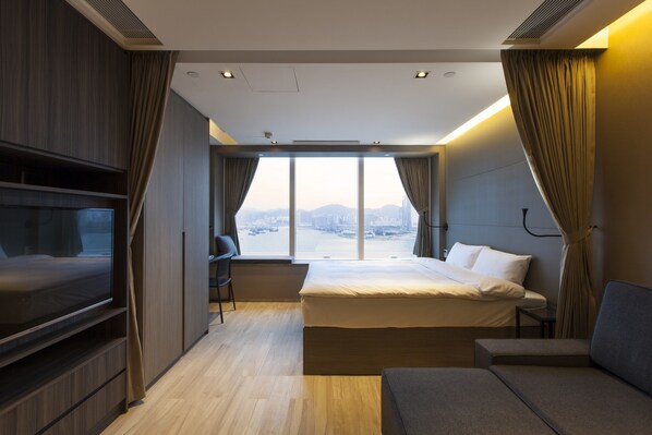 Una habitación de hotel moderna con una cama grande, televisión, escritorio y vistas a un paisaje urbano.