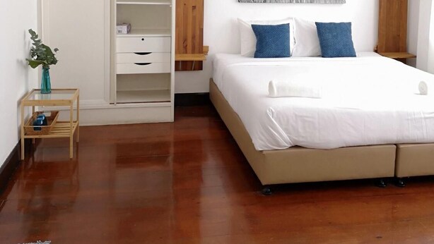Un dormitorio con cama, armario, una mesita con una planta y un cuadro colgado en la pared.