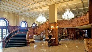 En storslagen entréhall med ett marmorgolv, en trätrappa, kristallkronor och en stor spegel.