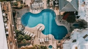 Ett flygbildsbild av ett semesterområde med en stor pool, solstolar och ett litet vattenfall.