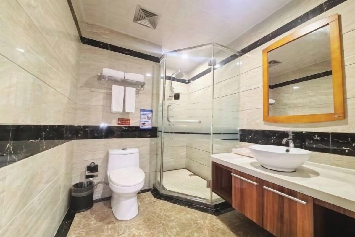 A modern bathroom with a glass shower enclosure, a white toilet, a wooden vanity with a white sink, and a large mirror.
