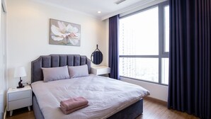 A modern bedroom with a large bed, a bedside table with a lamp, a wall-mounted mirror, and a window with curtains.