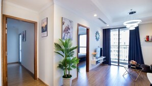 A modern apartment with a wooden floor, a potted plant, a TV, and a balcony with curtains.