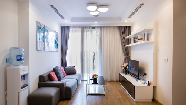 A modern living room with a sofa, a coffee table, a water dispenser, a TV, and a bookshelf.