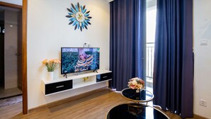 A modern living room with a flat-screen TV, a decorative wall clock, and a small table with flowers.