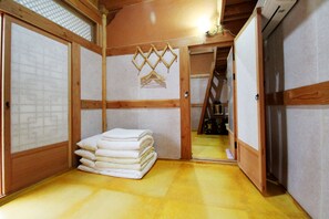 A traditional Japanese-style room with tatami flooring, a stack of white towels, and sliding doors. - Doldam House (Jeonju)