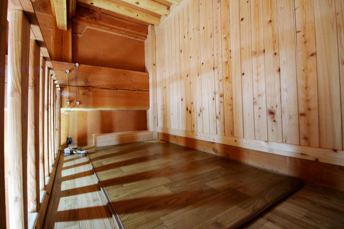 A room with wooden walls and floors, a visible electrical outlet, and a wooden door.