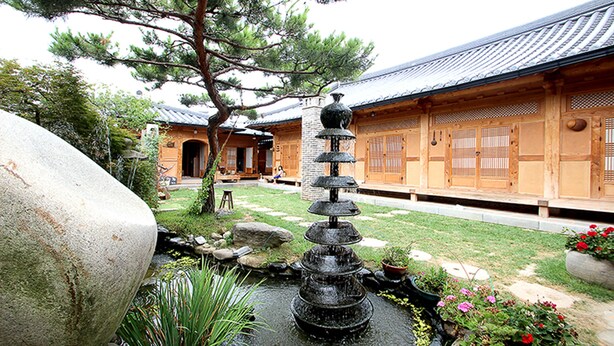 A traditional Japanese building with a stone water feature and a pine tree in the foreground. - Doldam House (Jeonju)